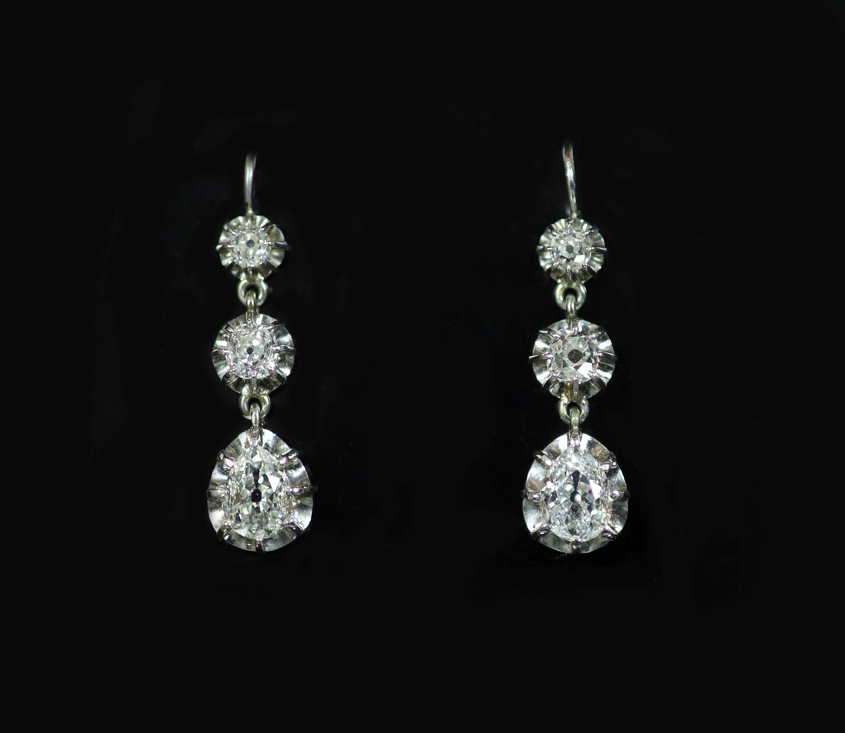 A pair of white gold, and graduated illusion set three stone old round and pear cut diamond drop earrings